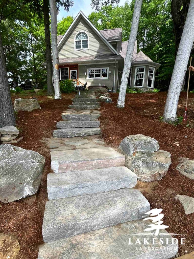 Stone steps through mulch and trees up to lakehouse